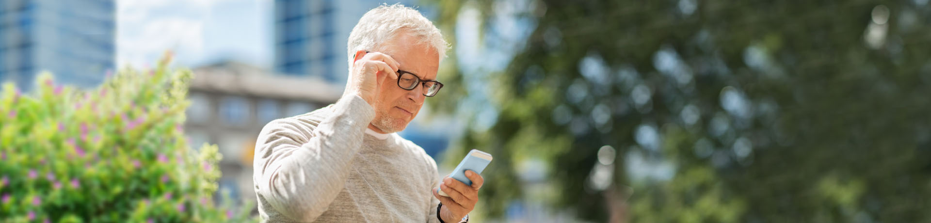 Man in a beige shirt and glasses looking at a mobile phone